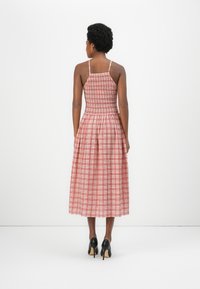 Rochie maxi cu model în carouri roșii și albe, cu bust smocat și bretele subțiri, fustă evazată, asortată cu pantofi cu toc înalt negri.