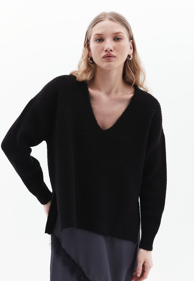 Maglione nero lavorato a maglia con scollo a V profondo, maniche lunghe oversize e un motivo testurizzato. Presenta delle fessure laterali all'orlo per un tocco di particolarità.