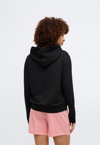 Fekete kapucnis pulóver, laza fazonnal, puha tapintással. Párba állítva mintás rózsaszín rövidnadrággal, amelyen kicsi szívminták vannak.