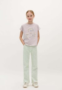 Lichtpaarse T-shirt met korte mouwen met een schedelafbeelding; mintgroene broek met een subtiele luipaardprint; witte sneakers.