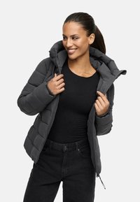 Veste d'hiver grise matelassée avec capuche, dotée d'une fermeture éclair et de poignets élastiques. Portée sur un haut noir et un jean noir.