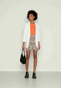 Blazer branco, top laranja, saia curta com padrão, bolsa preta e sapatos pretos. A saia apresenta um design abstrato em tons neutros.