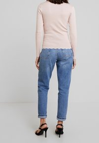 Světlé růžové pruhované tričko s dlouhým rukávem a vroubkovaným lemem, doplněné volnými modrými džínami. Doplňky zahrnují černé páskové sandály na podpatku.