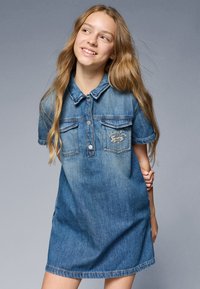 Abito di jeans con scollo a collare, maniche corte, due tasche sul petto e dettaglio con logo. Colore azzurro chiaro con effetti di scolorimento.