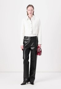 Veste cropped blanche, pantalon large en cuir noir, tenant un petit sac à main rouge. Textures lisses avec un design structuré.