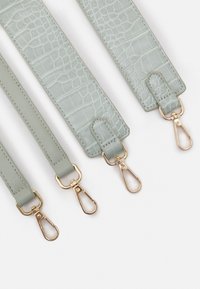 Světlé zelené umělé kožené popruhy s krokodýlí texturou, s kovovými klipy ve zlatém odstínu a hladkými okraji. Jsou viditelné tři různé délky.