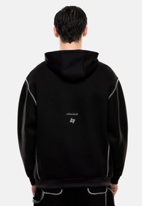 Felpa nera con finitura testurizzata, dotata di cappuccio, accenti riflettenti e logo stampato sul retro. Design semplice con cuciture visibili.