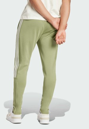 Pantaloni sportivi verde chiaro con strisce bianche ai lati, vestibilità slim e tessuto testurizzato. Indossati con sneakers bianche, la persona ha le mani unite dietro.