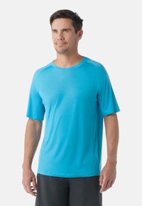 T-shirt de sport turquoise à manches courtes, col rond et texture lisse. Assorti à un short noir, créant un look contrasté.