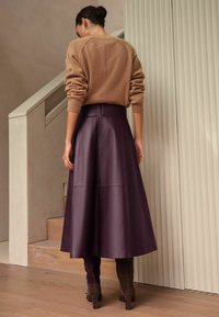 Suéter ajustado color marrón claro con puños acanalados, combinado con una falda de cuero color ciruela hasta el suelo que presenta costuras horizontales y un diseño acampanado.