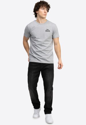 Grå bomulds t-shirt med rund hals og logo foran; parret med sorte denim jeans og hvide sneakers, hvilket skaber et afslappet outfit.