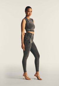 Harmaa farkk crop-top, jossa on teksturoidut olat, yhdistettynä korkeavyötäröisiin harmaisiin farkkuleggingseihin, joissa on paneelikuviointi ja tiukka siluetti.