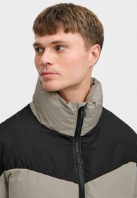 Gevoerde jas met een hoge kraag; kleurblokontwerp in zwart en beige; beschikt over een ritssluiting aan de voorkant en subtiele logo-gegevens op de borst.