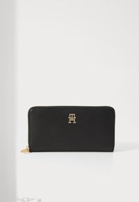 Black leather wallet with a textured surface, gold hardware, and a prominent logo on the front. Features a zip closure.