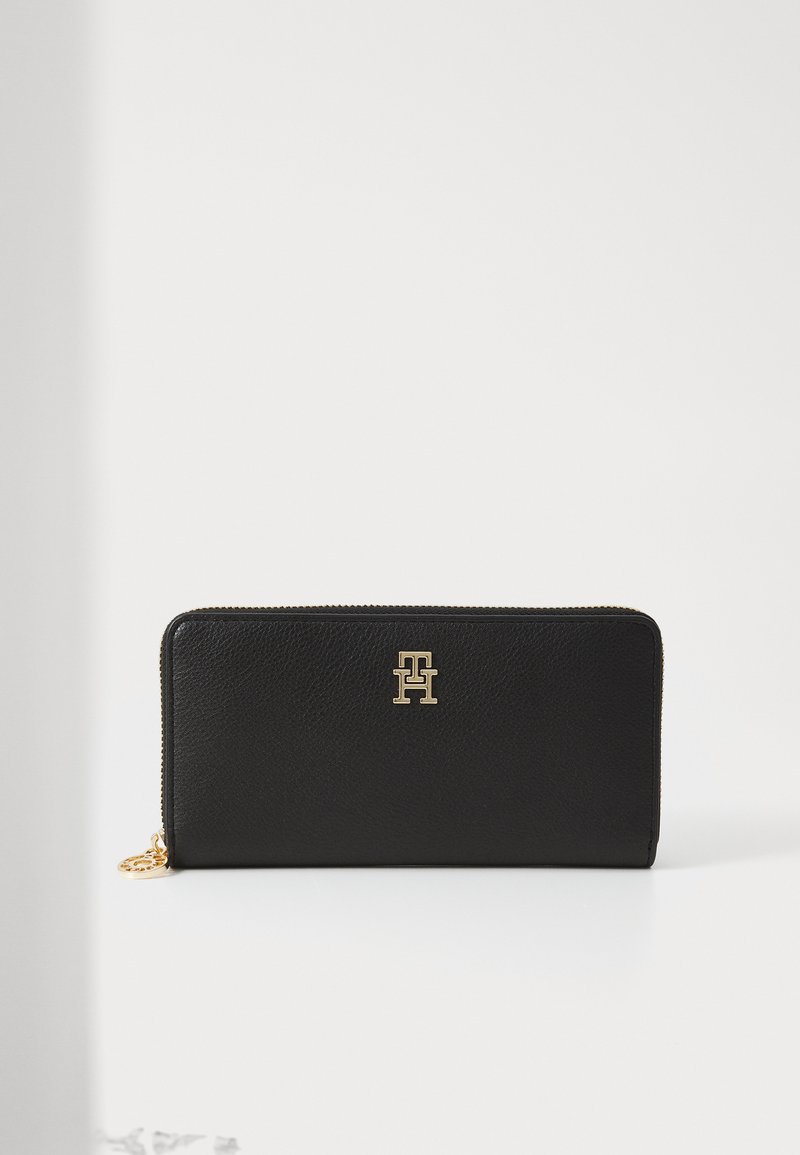 Portafoglio in pelle nera con superficie texturizzata, hardware dorato e un logo prominente sul davanti. Presenta una chiusura con zip.
