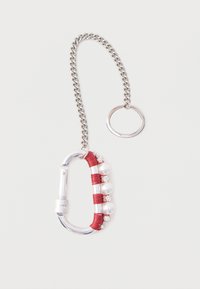 Hõbedane karabiinkonksuga võtmehoidja, mille ühe külje ümber on punast niiti, kaunistatud vahelduvate pärlite ja väikeste läbipaistvate rhinestone'idega, kinnitatud hõbedase kettiga.