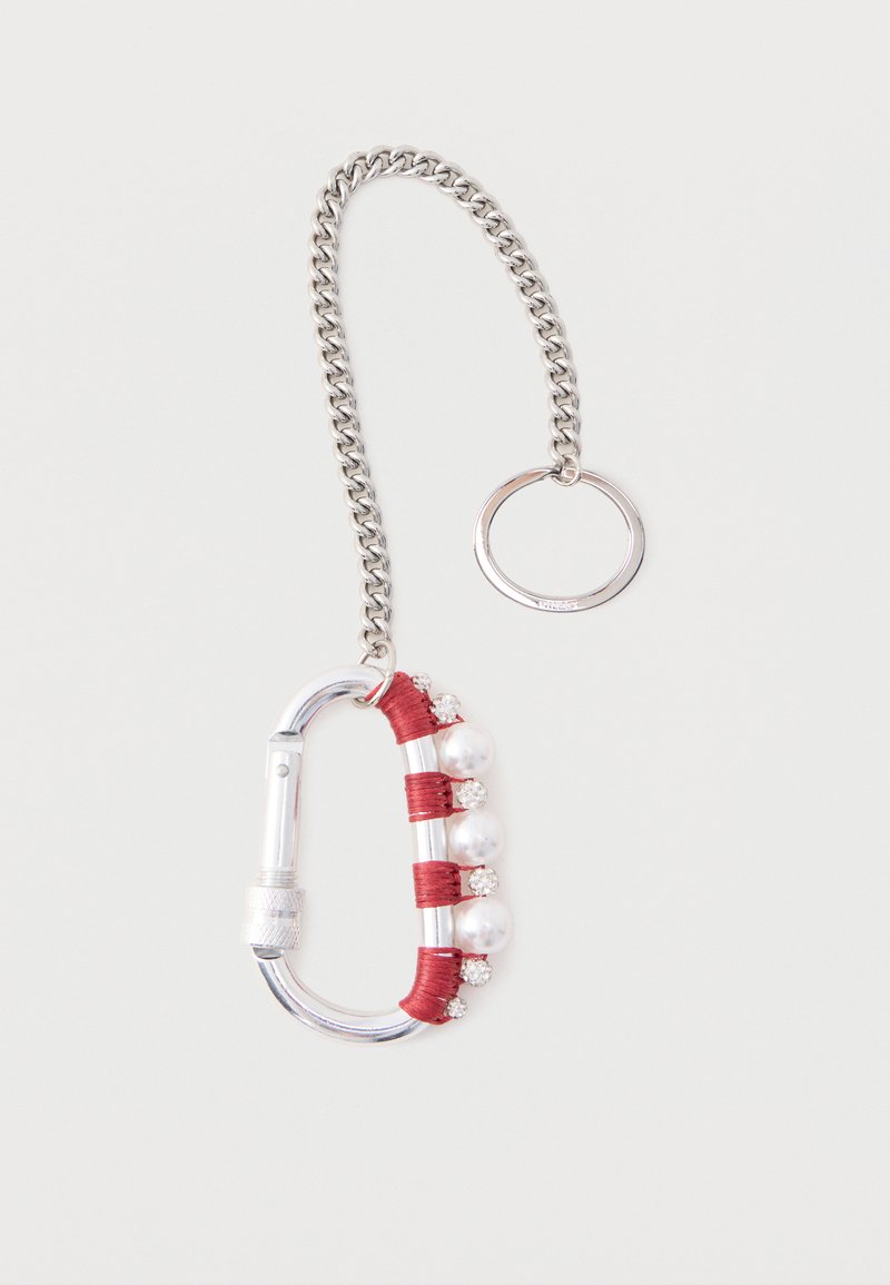Hõbedane karabiinkonksuga võtmehoidja, mille ühe külje ümber on punast niiti, kaunistatud vahelduvate pärlite ja väikeste läbipaistvate rhinestone'idega, kinnitatud hõbedase kettiga.