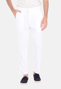 Pantaloni di lino bianchi con vestibilità comoda, dotati di pinces frontali, tasche laterali e una cintura elastica con cordino. Abbinati a espadrillas blu navy.