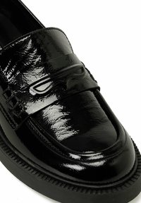 Black patent leather loafers with a textured finish, featuring a decorative strap and raised accents, and a thick rubber sole with ridged detailing.