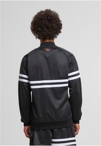 Giacca nera in satin con colletto a coste, accenti a strisce bianche sulle maniche e un logo a rombo marrone sul retro.