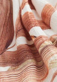 Woven fabric with a smooth texture features a pattern of orange and white horizontal stripes, showcasing intricate details in the weave.