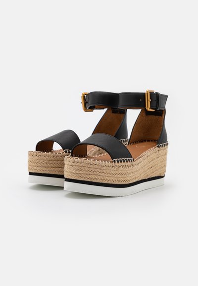 Svarte espadrille plattform sandaler har en vevd jute-såle, justerbar ankelrem med gullspenne, og design med åpen tå.