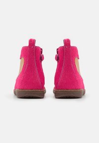 Bottes de cheville rose vif avec une texture pelucheuse, présentant des ouvertures latérales et une semelle marron texturée. De mini pampilles à l'arrière ajoutent du détail.