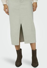 Lichtgroene midi-rok met een frontslit, gemaakt van zachte stof. Gecombineerd met donkerbruine suède enkellaarsjes met een decoratief patroon.