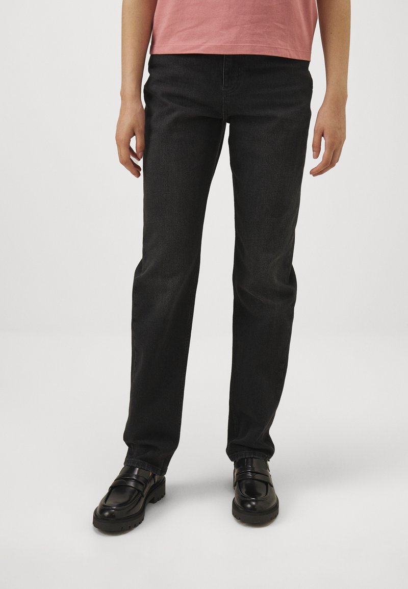 Vaqueros negros de corte recto, hechos de mezclilla, con una textura suave y diseño estándar de cinco bolsillos, combinados con mocasines negros.