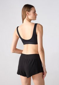 Reggiseno sportivo nero con spalline larghe e schiena bassa, abbinato a pantaloni corti neri coordinati con orlo a scallop e una texture morbida.