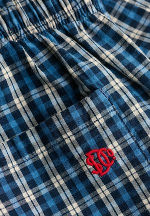 Blauw-wit geruite stof met een geplooide elastische tailleband en een klein rood geborduurd logo bij een gestikte zak.