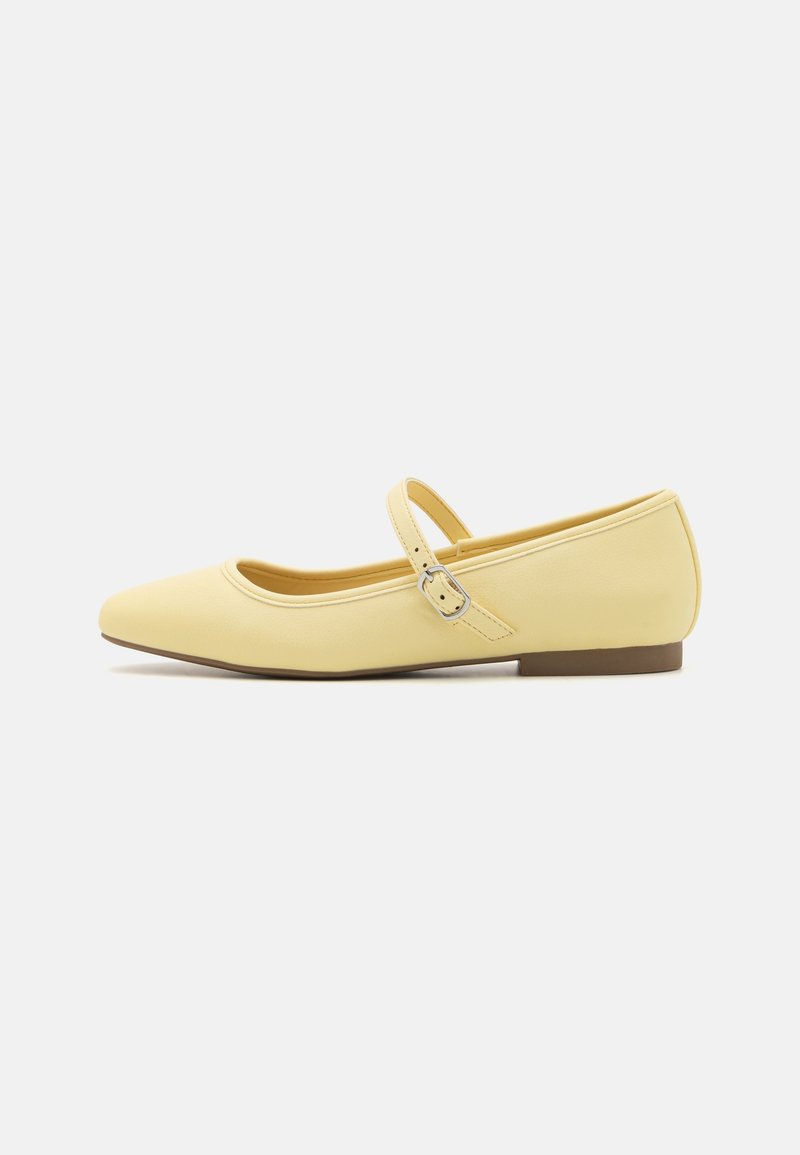 Zapato plano Mary Jane de cuero amarillo con punta afilada, strap con detalle de hebilla y tacón bajo marrón. Textura suave y diseño minimalista.