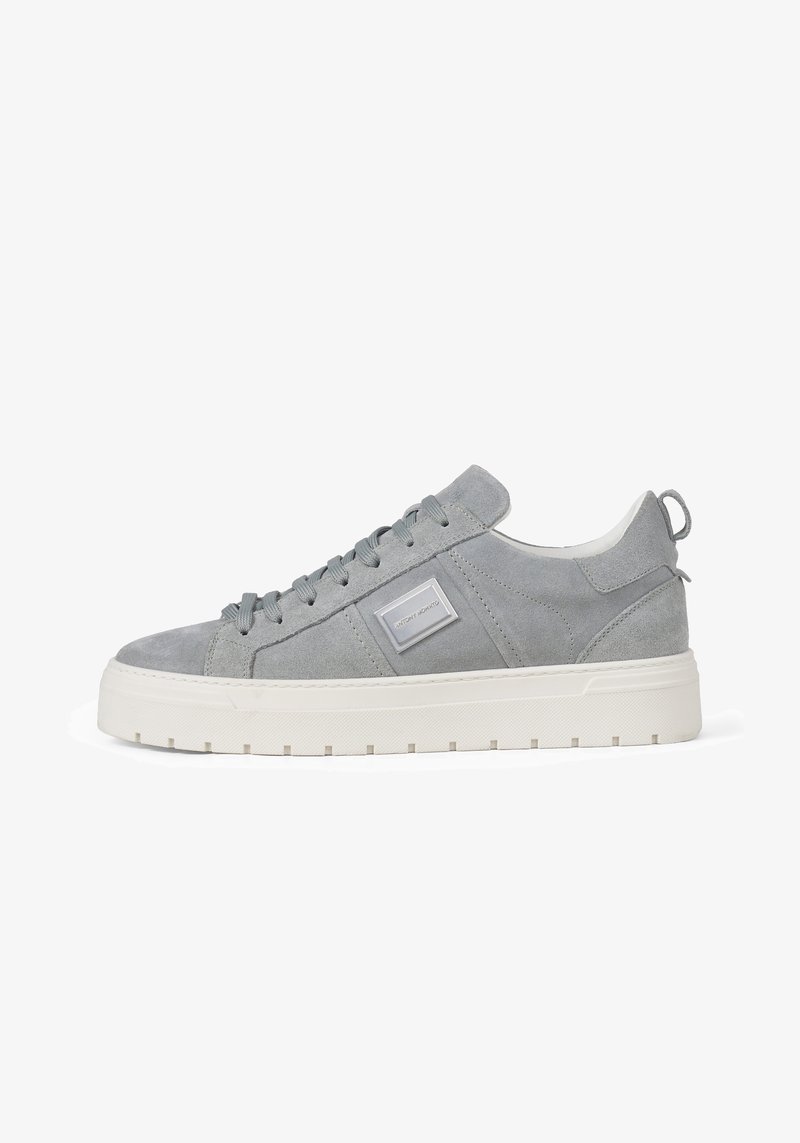 Low-top grijze suède sneaker met witte dikke rubberen zool, grijze veters en een rechthoekige logo-patch aan de zijkant.