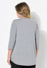 Maglietta grigia, morbida, a maniche lunghe con scollo rotondo e vestibilità rilassata. Presenta un orlo curvo e fessure laterali per un maggiore confort.