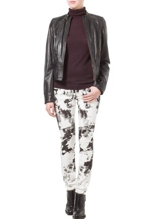 Veste en cuir noir, col roulé ajusté bordeaux et jean skinny blanc avec un motif abstrait noir. Des bottines noires complètent la tenue.