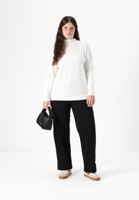 White long-sleeve top with a high neck, paired with black wide-leg pants, black handbag, and white sneakers with beige soles.