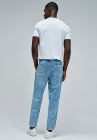 Camiseta blanca de manga corta combinada con jeans de denim azul claro que cuentan con dos bolsillos traseros y un ajuste relajado. Zapatillas blancas completan el look.