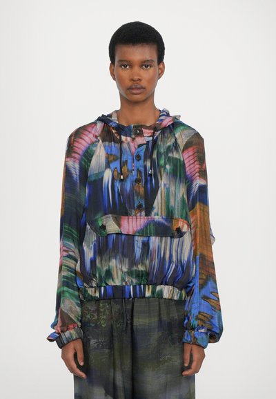 Veste colorée et légère avec une capuche, présentant un mélange de motifs bleus, verts et roses, avec des fermetures à boutons et des poignets élastiques.