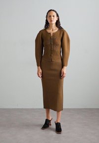 Bruine gebreide jurk met geribbelde textuur, aansluitende bodice, knopen sluiting en lange mouwen, gecombineerd met zwarte open teen hakken.