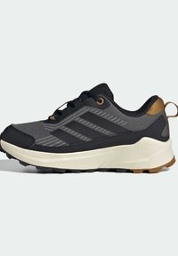 Chaussure de course noire et grise avec une tige en maille texturée, un design à trois bandes, une semelle en caoutchouc et un accent beige au talon.
