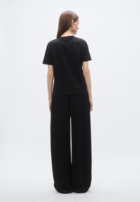 Svart bomulls-T-skjorte med korte ermer og rund hals, kombinert med vide, svarte bukser. Jevn tekstur, minimalistisk design og ensfarget.