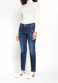 Smala jeans i mörkblå denim, med en midjehöjd i mellanläge, slitna detaljer och kontrasterande sömmar. Kombineras med vita sneakers.