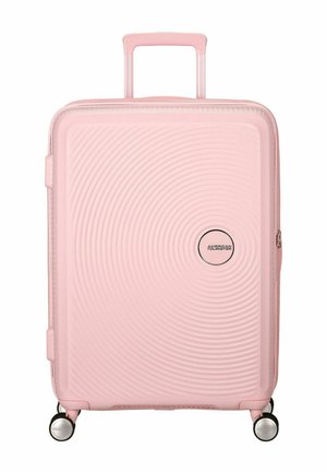 Maleta rígida rosa con un diseño acanalado, manija retráctil, cuatro ruedas y un detalle de logotipo redondo. Textura suave y ligera.