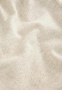 Jasnobeżowa tkanina o miękkiej, teksturowanej powierzchni, z delikatnymi różnicami w kolorze i równomiernym, lekko zużytym wyglądzie.