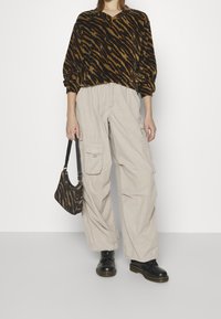 Sweat-shirt à rayures marron et noires, pantalon cargo beige ample, bottines noires et petit sac à main à motifs. Texture lisse, coupe décontractée.