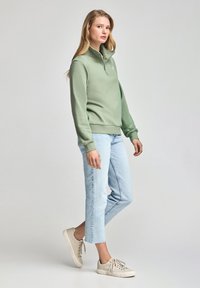 Ljusgrön kvartsgammal zip-pullover, mjukt tyg, ribbade ärmslut, i kombination med ljusblå cropped jeans och beige sneakers. Enkel design, avslappnad passform.
