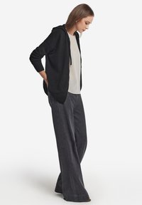 Czarny kardigan z kapturem noszony na jasnej górze, w zestawieniu z szerokimi szarymi dżinsami. Stylizacja charakteryzuje się luźnym krojem i miękkimi teksturami.