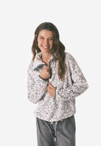 Fleece-pullover i hvid med sorte leopardpletter, med høj krave og lynlås, parret med grå joggebukser med snørre.