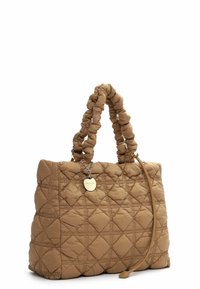 Quilted brown tote bag with padded handles, diamond stitching, a gold circular charm, and an attached thin strap on a white background.