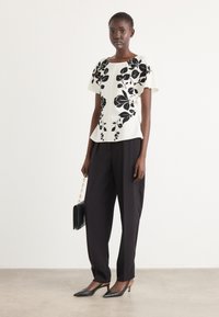 Witte top met zwarte bloemenprint, peplum stijl, gecombineerd met losse zwarte broek en zwarte puntige hakken. Eenvoudige zwarte handtas met kettingband.